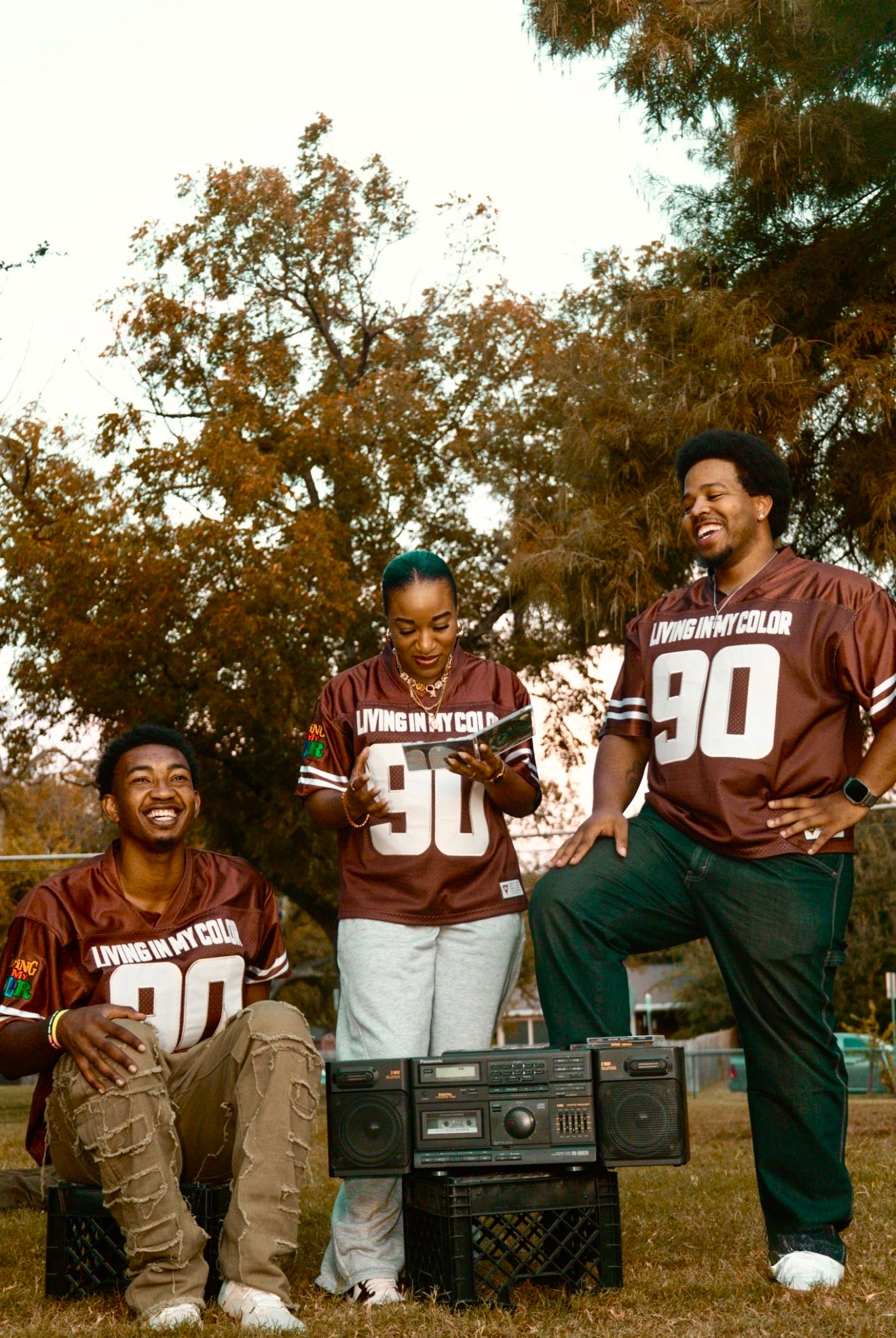 Three people in matching brown sports jerseys with the number 90, sitting outdoors with trees in the background.