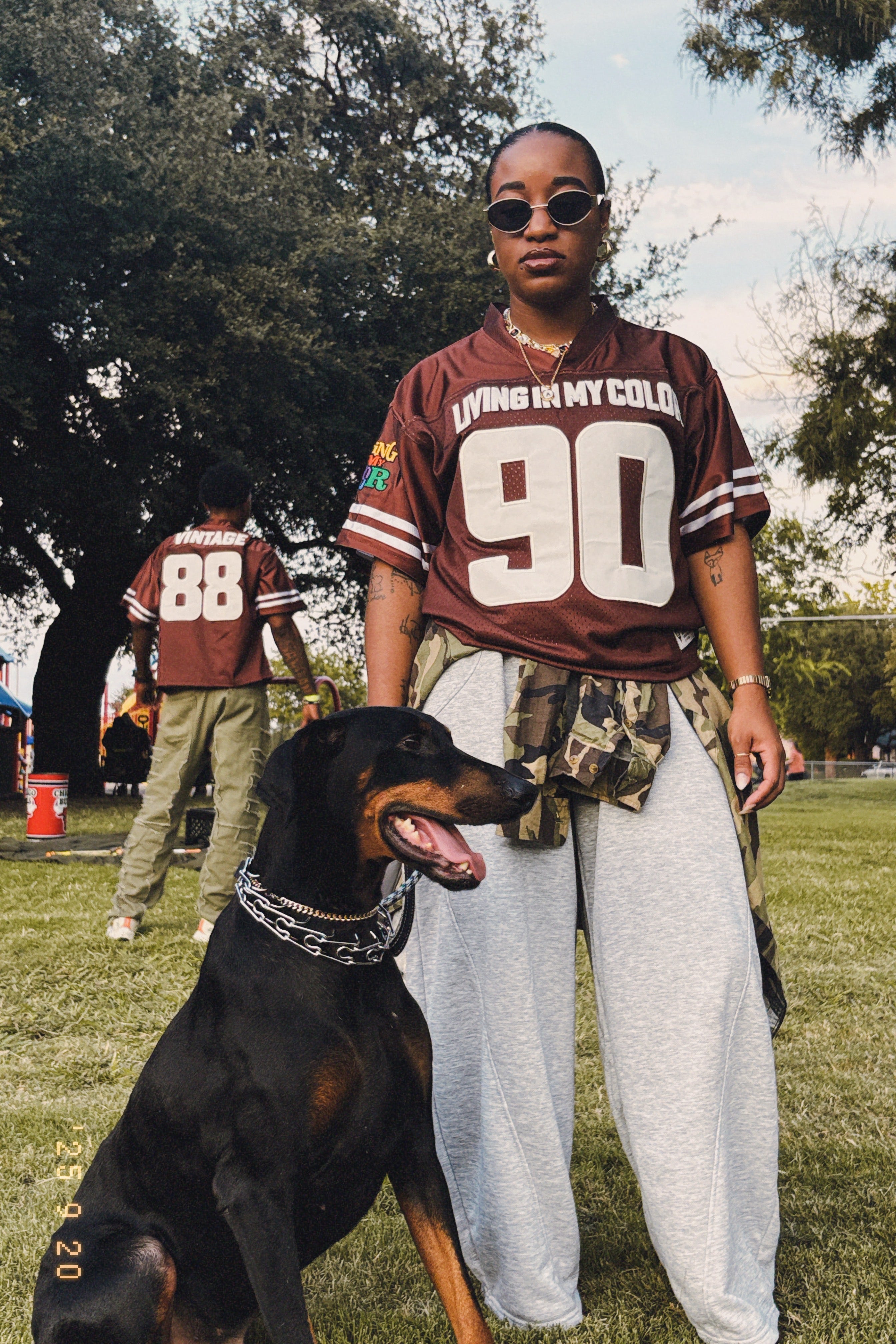 Black woman wearing a sports jersey with a Doberman on a grassy field